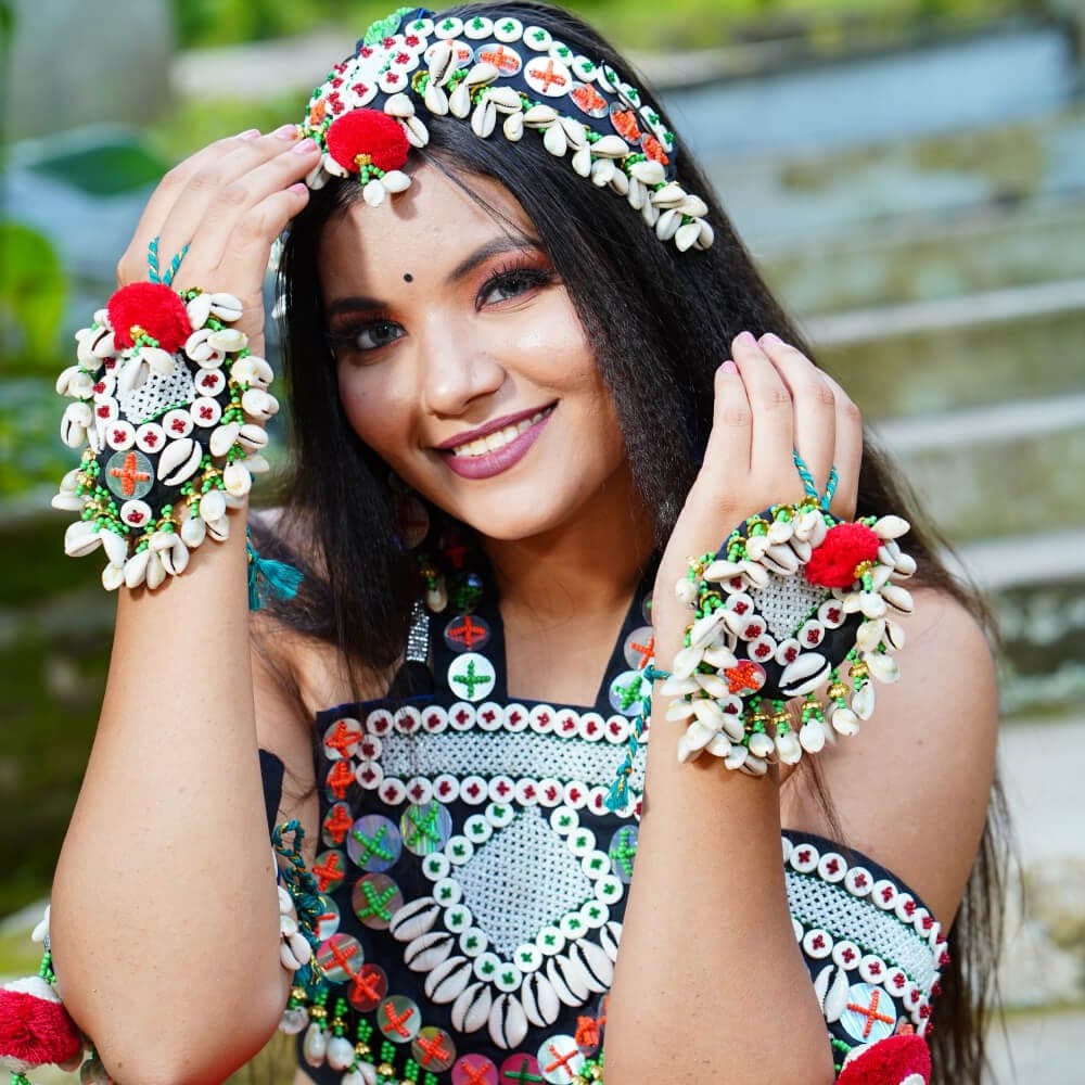 A smiling woman wearing a cowrie shell headband and matching hand pieces