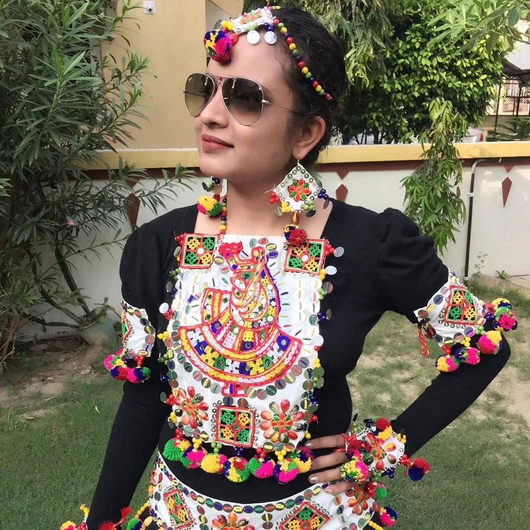 A woman in sunglasses wearing a colourful pom-pom headband, earrings, and an embroidered Navratri yoke