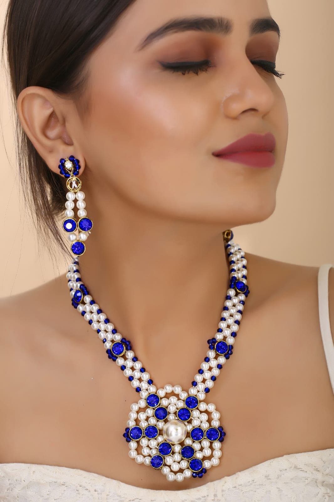 A blue and pearl necklace with matching earrings, worn by a model