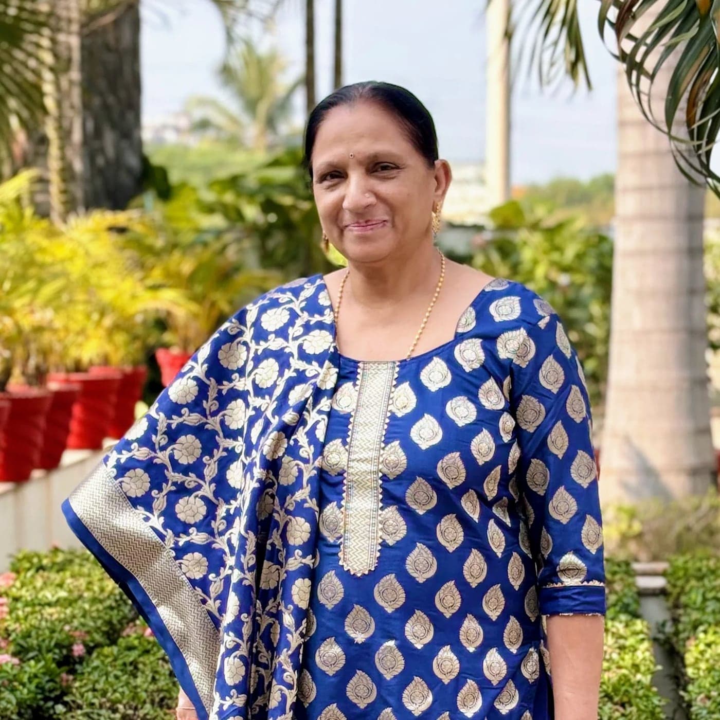 Portrait of Sharda Jadhav in a blue and gold suit, standing in a garden